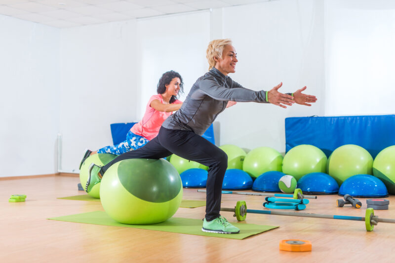 Mulher ativa de meia-idade trabalhando com bola de estabilidade participando da aula de fitness em grupo.