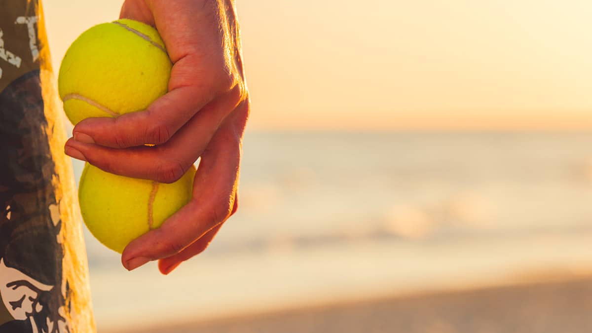 Homem segurando bolas de tenis na praia