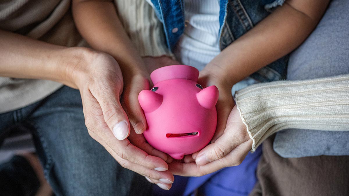 Várias mãos a segurar um cofrinho de porquinho rosa