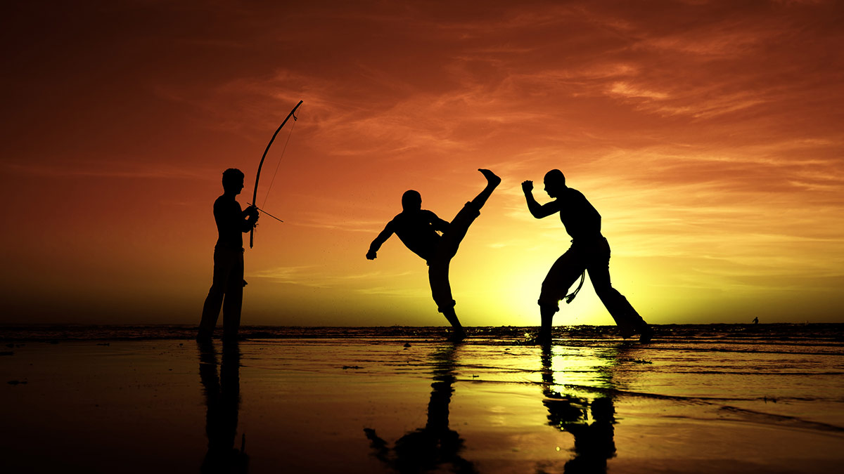 Pessoas praticando capoeira em praia ao pôr do sol