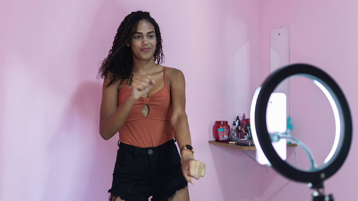 Jovem mulher fazendo gravando uma dança utilizando seu smartphone com ringlight