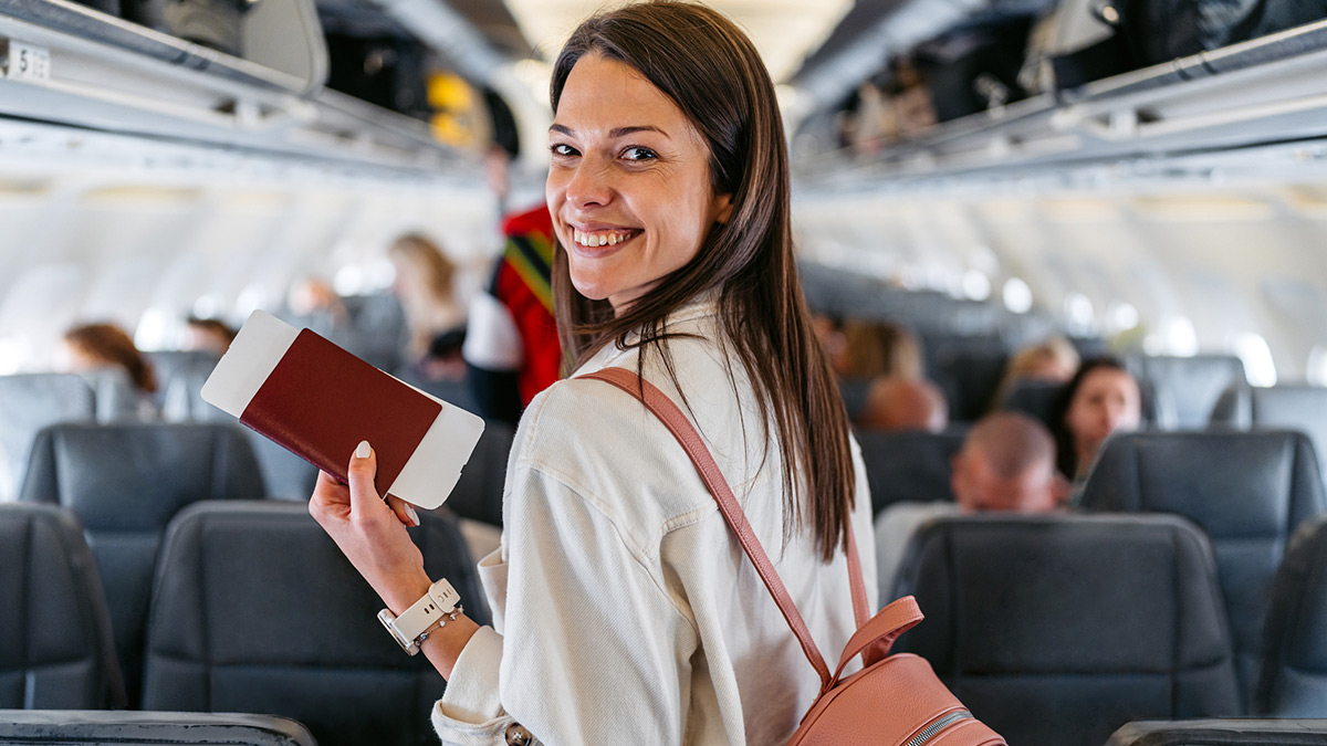 Mulher em pe no avião segurando passaporte sorrindo