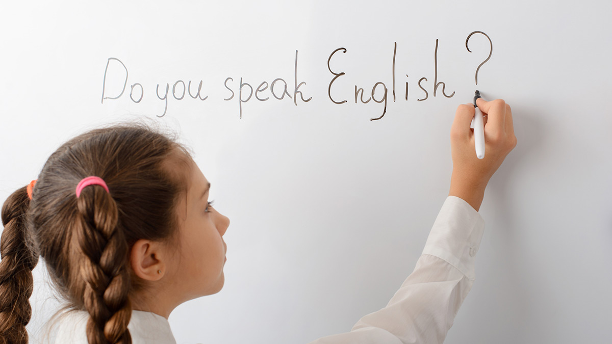 Menina escrevendo em uma lousa branca em inglês a frase "Do you speak English?"