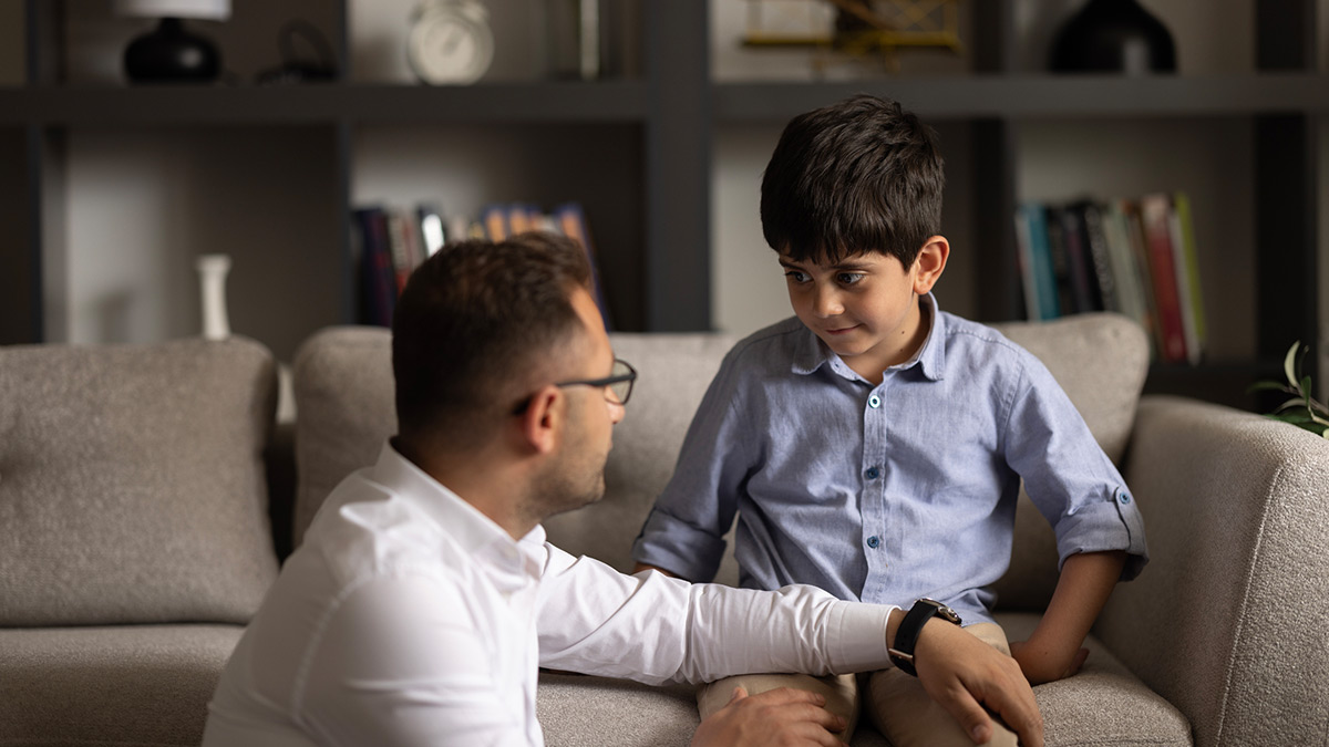 Pai dando conselho ao filho que está sentado no sofá
