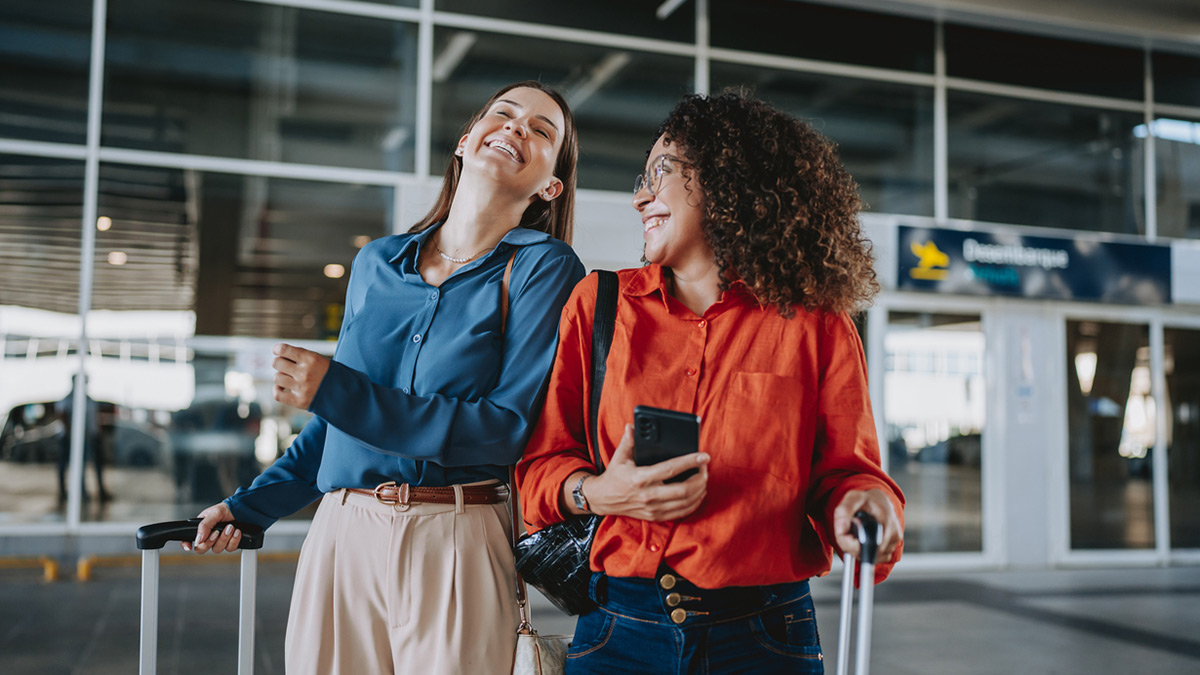 Duas amigas a sorrir em frente a um aeroporto