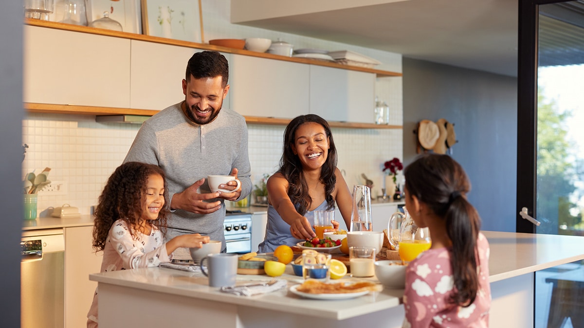 Família reunida tomando café da manhã na cozinha, sorrindo e aproveitando o momento juntos.