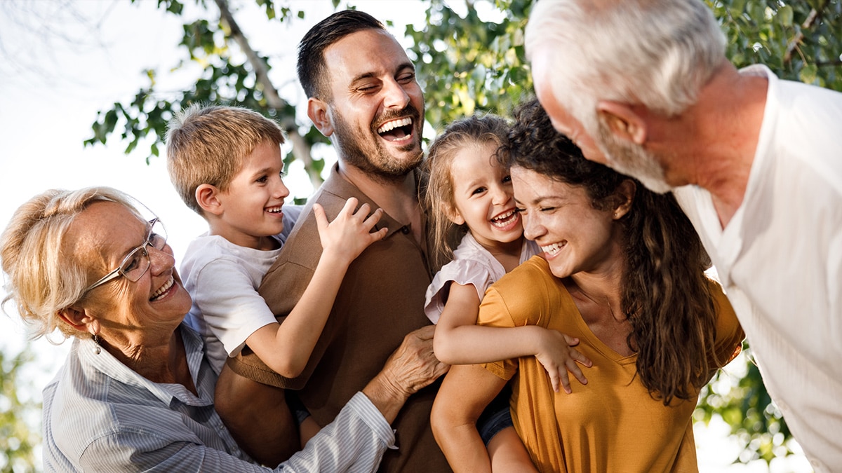 Família multigeracional sorrindo e se abraçando em um momento de alegria ao ar livre.