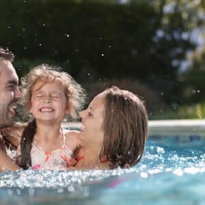 Pai, mãe e filha se divertindo juntos na piscina em um dia ensolarado.