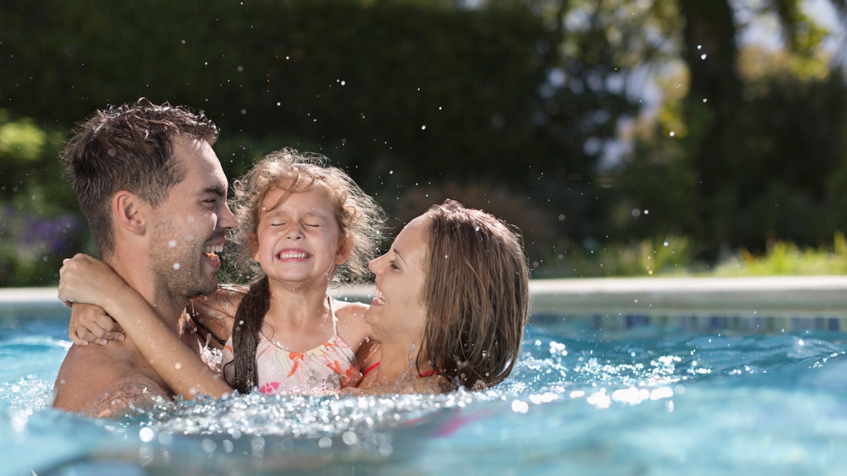 Pai, mãe e filha se divertindo juntos na piscina em um dia ensolarado.