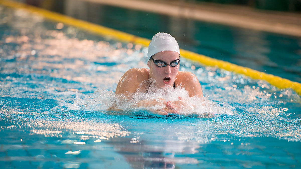 Nadadora em prova de natação estilo peito durante competição oficial em piscina olímpica